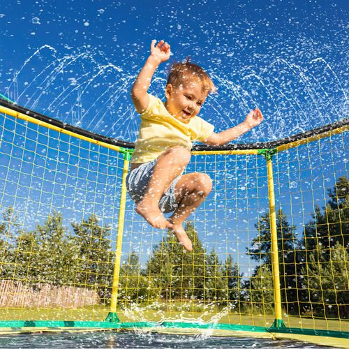 Child jumping through sprinkler mist on trampoline during outdoor therapy session.”