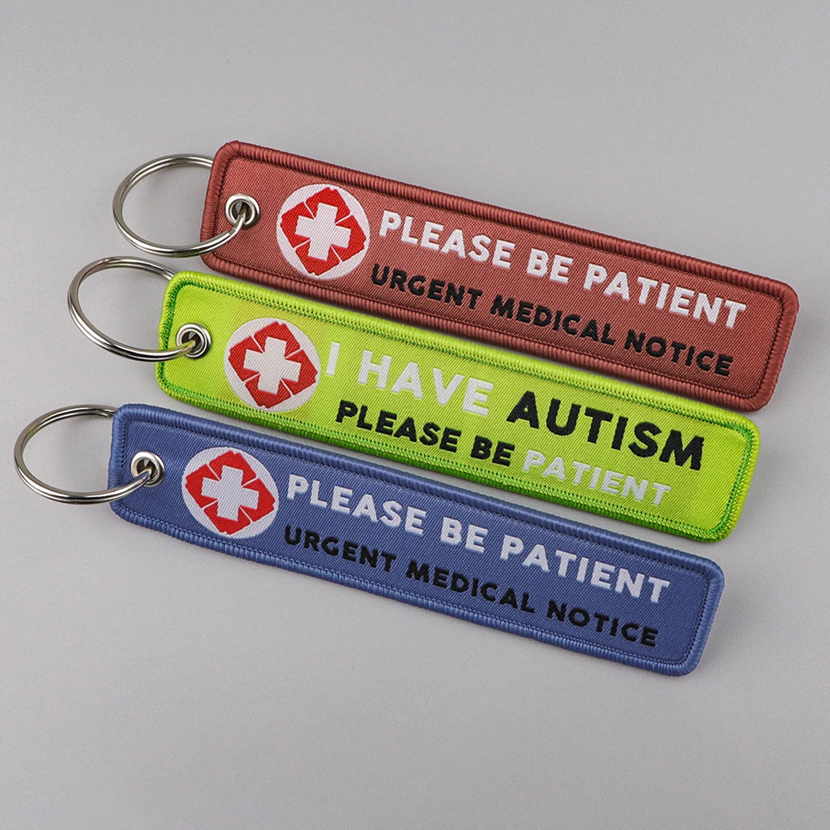 Three keychains with medical and autism awareness messages on a gray background