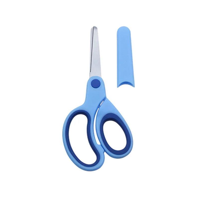 Left-handed children’s scissors in soft colour shown beside protective sleeve on desk with craft paper pieces