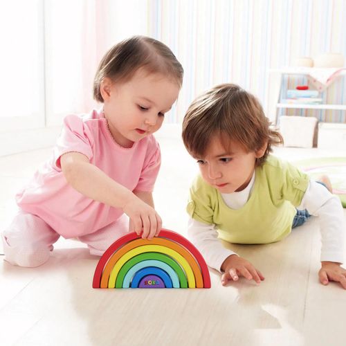 Two children playing with a wooden rainbow toy on a light-colored floor.