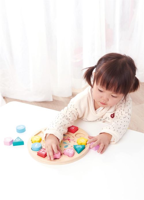 Child placing numbered block into clock face, practising coordination and early time recognition
