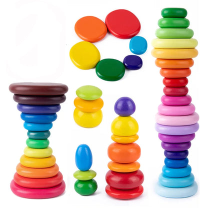 Wooden rainbow pebbles stacked in gentle tower on soft play mat, various shapes and colours scattered beside for sensory building activities