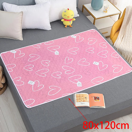 A pink waterproof changing pad with white hearts pattern, laid out on a bed next to a book and a plush toy.