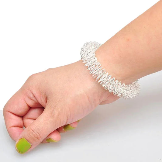 Pair of metallic wrist massage bracelets resting on fabric pouch, designed for acupressure-based stress relief and sensory regulation