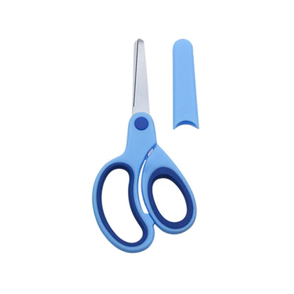 Left-handed children’s scissors in soft colour shown beside protective sleeve on desk with craft paper pieces