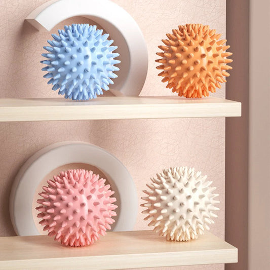 Four textured balls in blue, orange, pink, and white on a shelf against a beige wall.